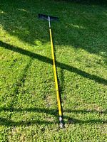 Full length view of yellow pole snow pusher with black blade shown assembled on grass
