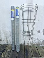 Two sealed rolls of Garden Zone hardware cloth next to two stacked tomato cages