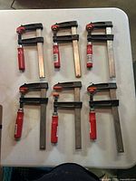 Six identical F-style bar clamps laid on table showing overall condition