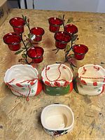 Top view of five ceramic stocking planters and three holly tealight holders with six red glass cups