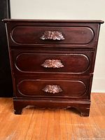 Front view of nightstand showing three drawers and carved pulls