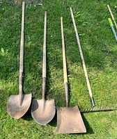 Four of the five long-handled tools laid on grass: two round shovels, one square spade, one garden rake