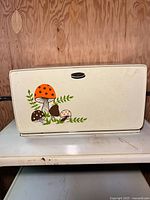 Front view of closed cream metal bread box with mushroom decal