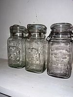 Three square clear glass quart jars with embossed text and wire bails