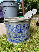 Front view of galvanized Fenwick Woodstream minnow bucket with handle up and perforated lid visible