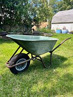 Side view of entire green plastic wheelbarrow on grass