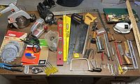 Overall lot on workbench showing power tools, hand saws, measuring tools, flashlight, wrenches and accessories