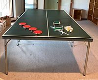 Overall view of green ping-pong table with four paddles and accessories on surface