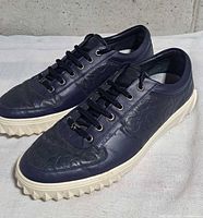 Oblique view of both sneakers showing embossed leather uppers and serrated soles