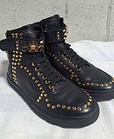 Oblique front view showing gold studs, laces, Medusa buckle