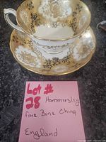 Teacup on saucer with handwritten lot note showing maker and material