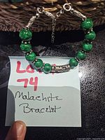 Bracelet laid flat on note card showing malachite beads, curved bar, clasp and extender