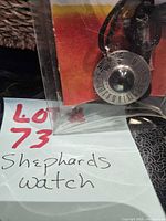 Pendant in plastic sleeve beside note showing lot number and handwritten title