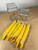 Front view of two square glass jars and eight folded yellow napkins