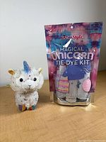 Front view of sealed Magical Unicorn Tie-Dye Kit pouch with plush unicorn beside it