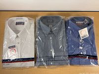Front view of three packaged dress shirts showing colors, brands, tags