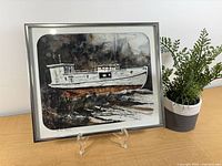 Full view of framed painting with stand and plant for scale