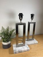 Pair of brushed nickel rectangular lamp bases on marble slabs with plant for scale