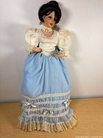 Front view of porcelain musical doll in blue and cream Victorian outfit