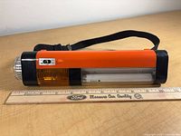 Left side view showing amber signal lens, battery compartment, wrist strap and ruler indicating length