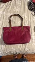 Full exterior front view of magenta leather tote with brown strap