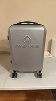 Front view of silver hardshell suitcase showing embossed Roberto Cavalli logo and spinner wheels