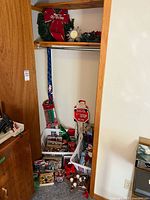 Closet view showing wreaths on shelf, baskets of ornaments, lights, Santa sign