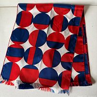 Full view of folded silk scarf showing geometric red, white and blue pattern and fringe