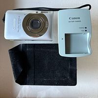 Canon PowerShot SD1300 IS camera front view with charger and case