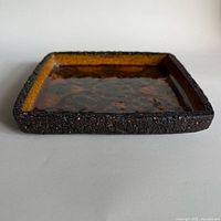 Oblique side view showing square form, textured clay rim, glossy interior