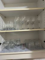 Cabinet shelves showing stemmed wine glasses, stemless wine glasses, lowball tumblers and faceted tumblers