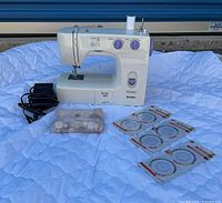 Full lot view showing Kenmore sewing machine, foot pedal, bobbin case, three pin wheel packages, white thread spool