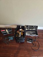 Overview of all items laid out: drill bit set, Makita sander, hand tools in tote, BBQ utensil case, jigsaw