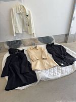 Four coats laid out: left black hooded, center cream, right black raincoat; ivory jacket hanging above