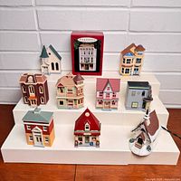 Full group of ten Hallmark Nostalgic Houses & Shops ornaments displayed on risers, showing nine loose buildings and one boxed ornament