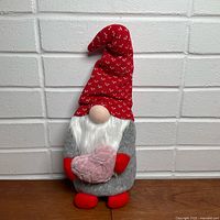 Front view of grey gnome with red heart-patterned hat holding pink heart