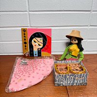 Group shot of all four items: doll, card, textile in sleeve, wooden box