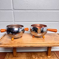 Front view of spherical chrome creamer and sugar with orange Bakelite handles and feet