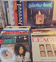 Two stacks of vinyl records showing front titles including Electric North, John Miles, Hightime, Human League