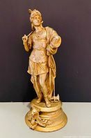 Full view of gold-tone cast metal figurine on plinth