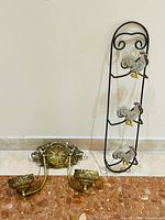Full view of both items: tall cast iron plate rack with rooster motifs and brass two-arm sconce