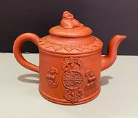 Full view of clay teapot showing overall form, spout, handle, and decoration