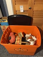 Orange plastic tote with jack-o-lantern graphic containing assorted Halloween items