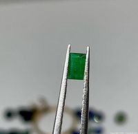 Emerald held in tweezers showing rectangular cut and colour