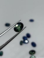 Tweezers holding oval teal sapphire front view