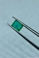 Emerald held in tweezers showing rectangular cut and green color