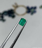 Emerald held by tweezers showing overall size and color