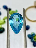 Close-up of faceted pear-cut blue topaz held in tweezers