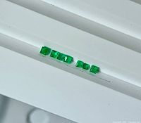 Seven square green gemstones aligned on white background