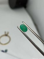 Close-up of one oval emerald held in tweezers